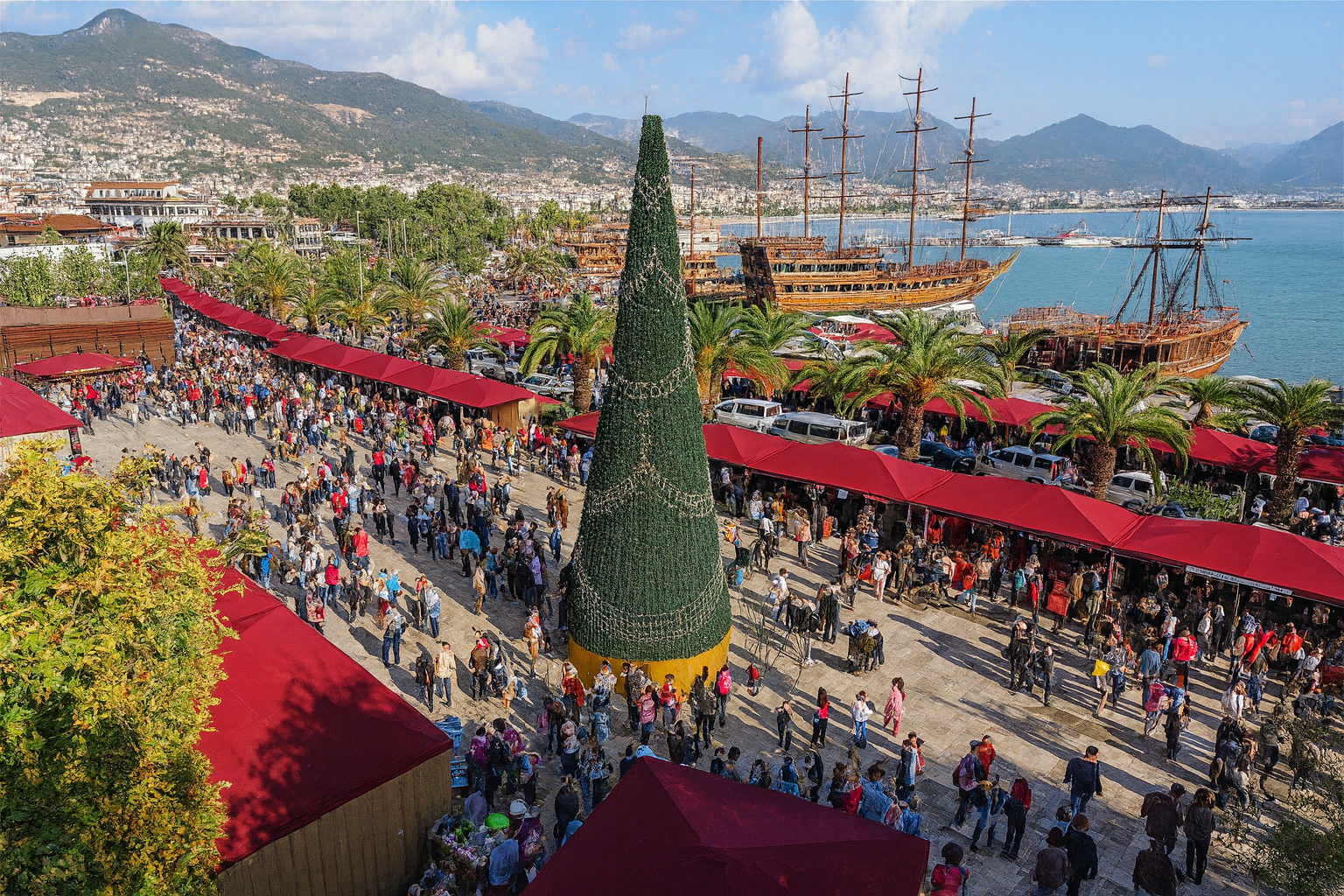 Alanya Weihnachtsmarkt 2025 mit großem Weihnachtsbaum, bunten Ständen und Blick auf den Hafen mit Piratenschiffen.